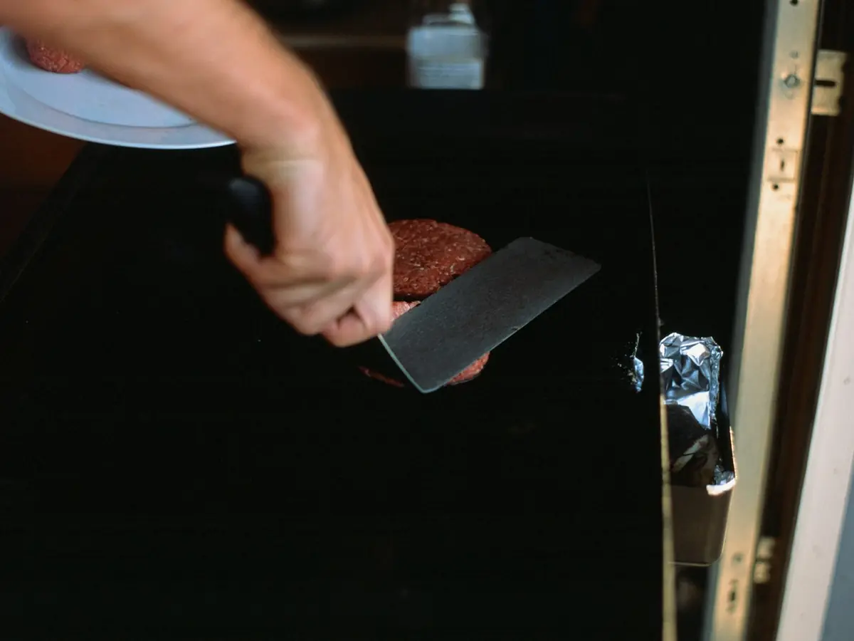 A beef patty being smashed flat on the griddle